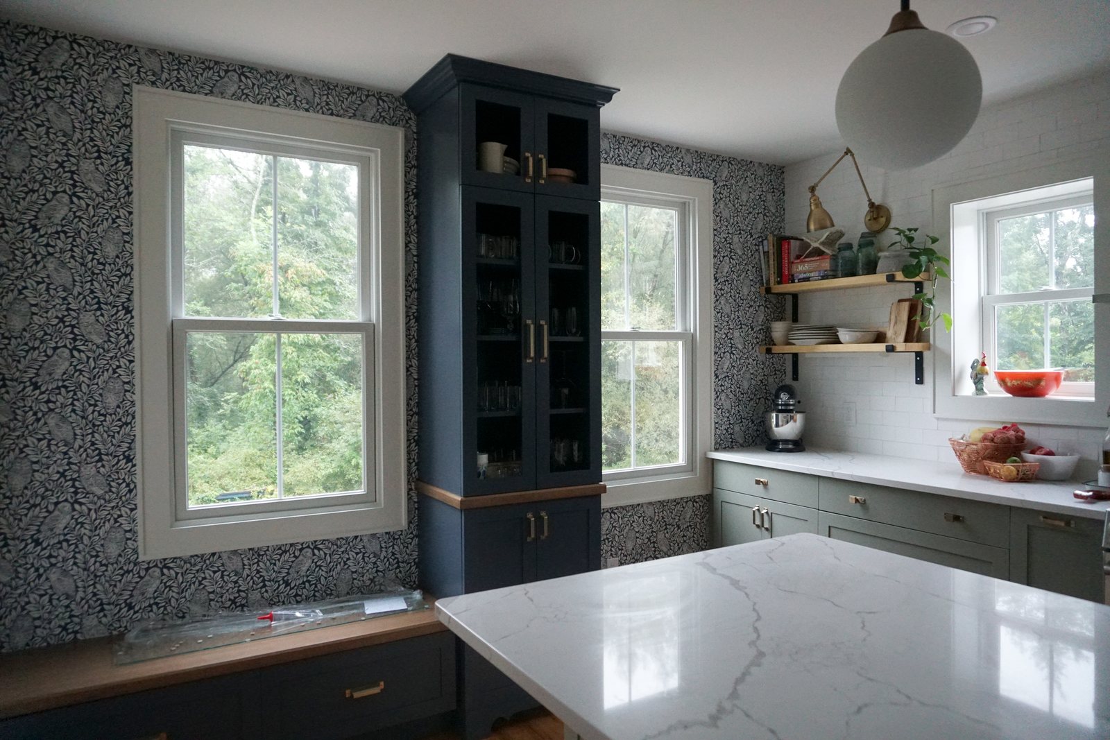 Renovated farmhouse kitchen with a navy glass-front cabinet, botanical wallpaper and marble island: 1790 Farmhouse Renovation, Milton NY